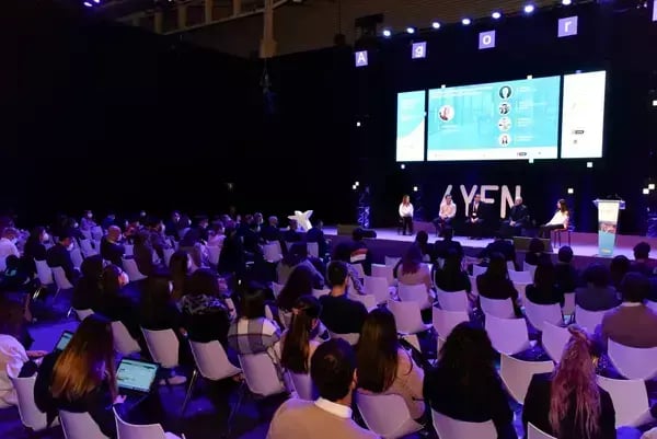 Audience attending a panel discussion at the 4YFN event, with speakers seated on stage and large presentation screens displaying speaker profiles and session details.