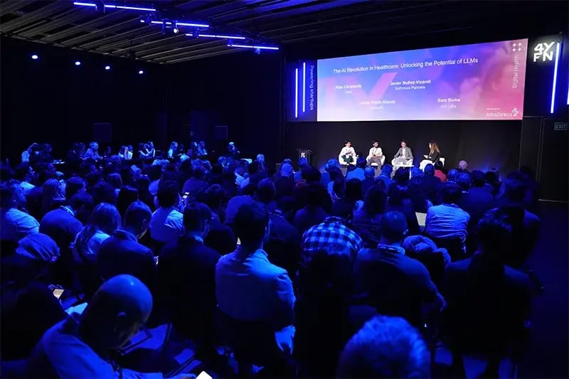 Large seated audience watching a panel titled 'The AI Revolution in Healthcare: Unlocking the Potential of LLMs,' with four speakers on stage under blue lighting.