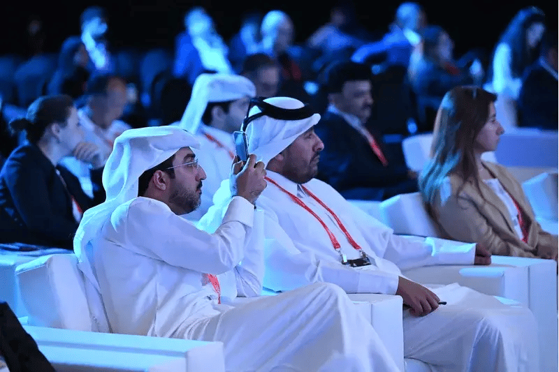 Audience members seated during a conference session at MWC Doha, including attendees in traditional Qatari attire listening to a speaker presentation.