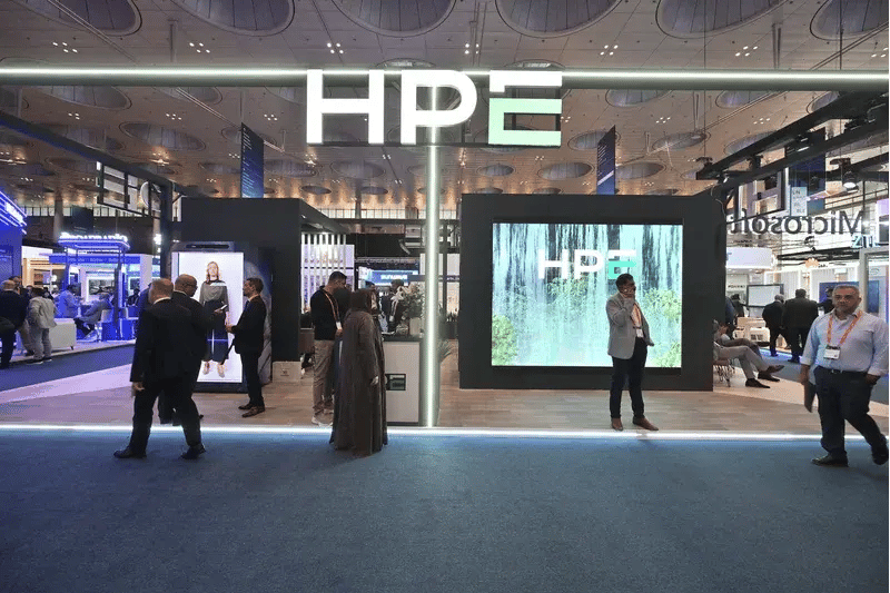 Front view of the HPE stand showcasing interactive screens, branding and technology demonstrations, with delegates engaging in discussions throughout the exhibition hall.