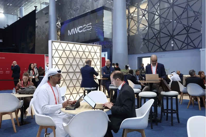 People at MWC25, an event with a modern setting, talking and working on laptops. The atmosphere is professional and collaborative.